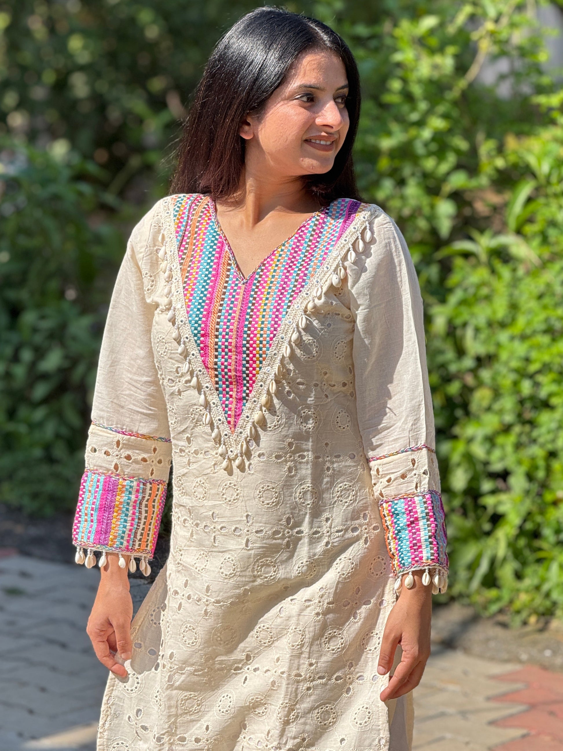 Woman wearing a cream-colored traditional outfit with colorful patterns in an outdoor setting.